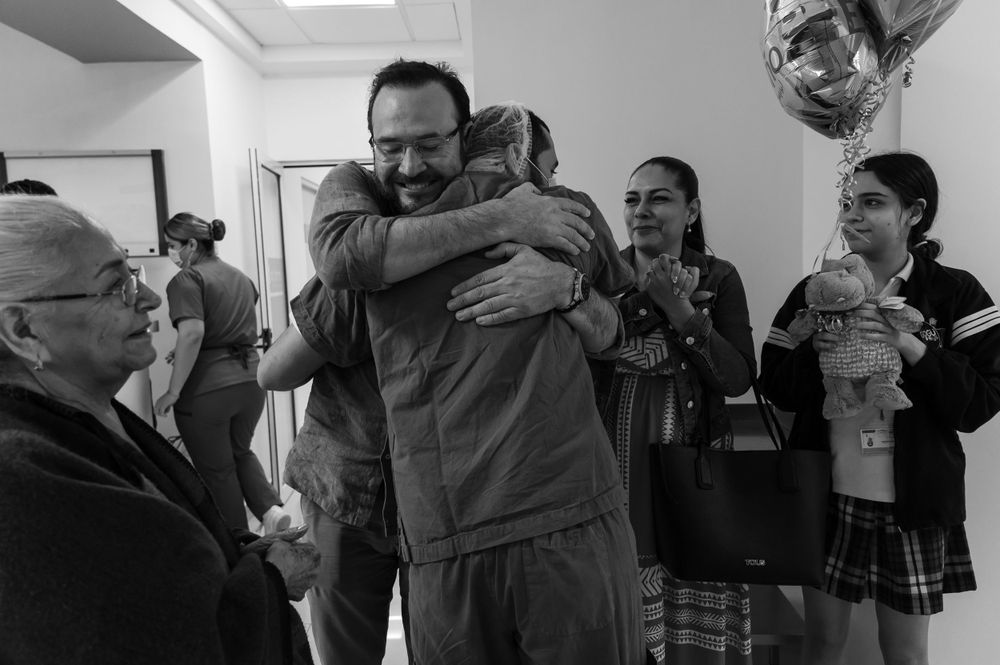 Group of people gathered in hospital corridor sharing emotional moment.