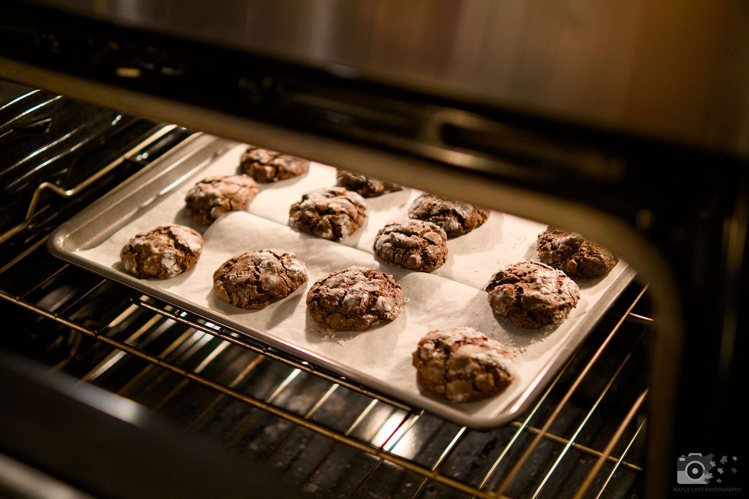Chocolate cookies arranged in rows on parchment paper baking in the oven.