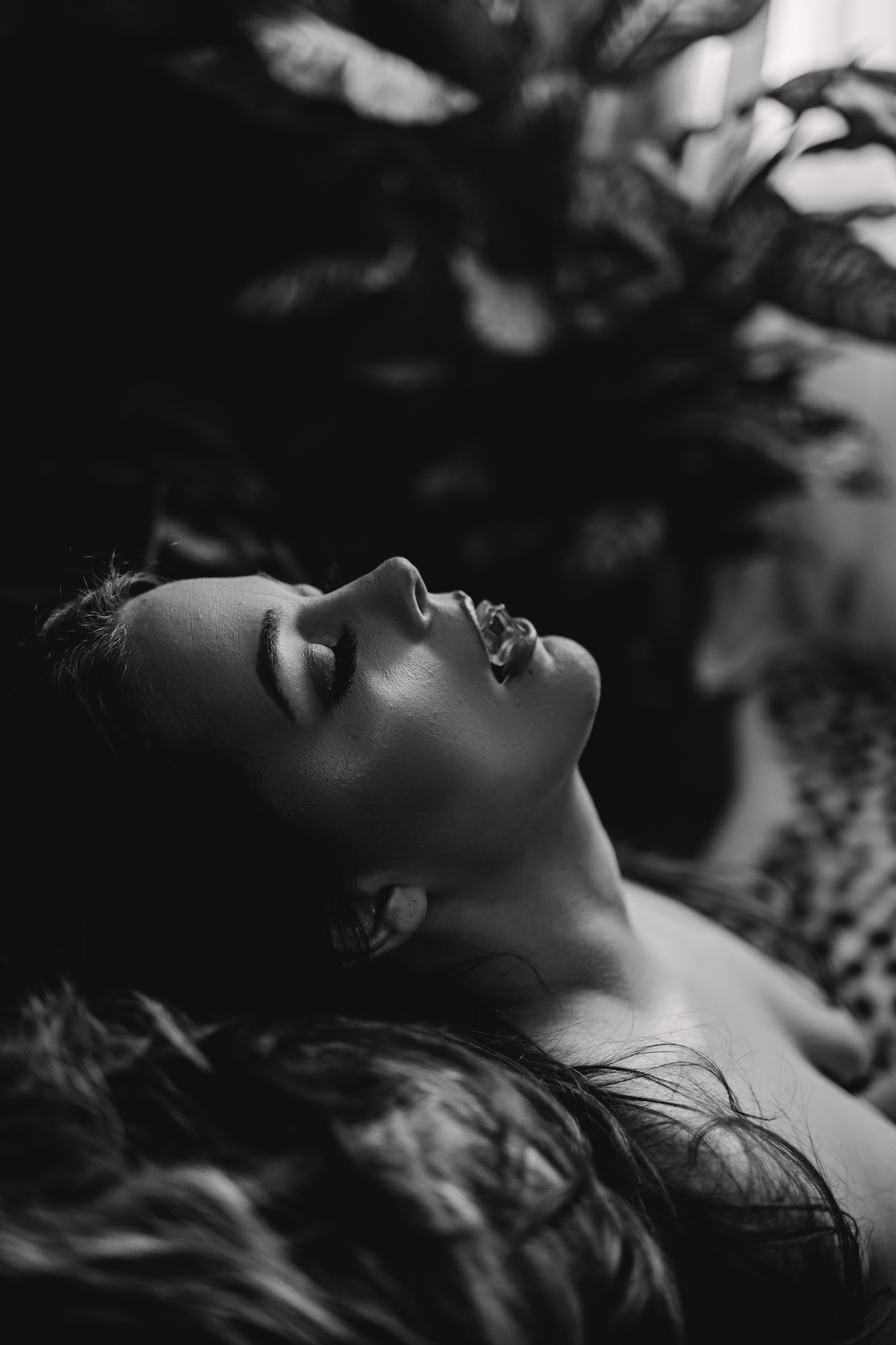 Black and white artistic portrait showing profile view resting against natural foliage background.