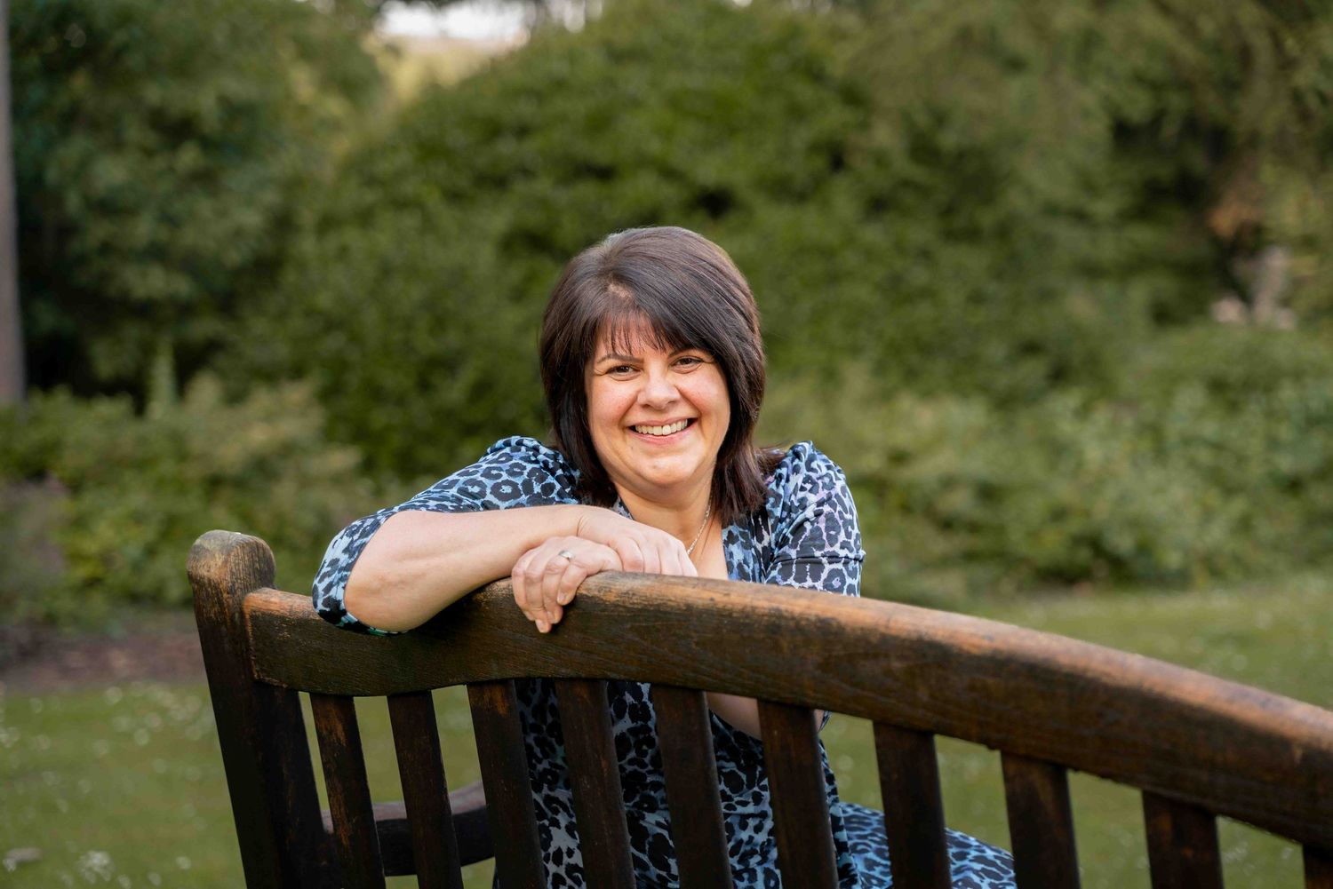 A person relaxes on a wooden garden bench surrounded by lush greenery. Lincolnshire branding photographer.