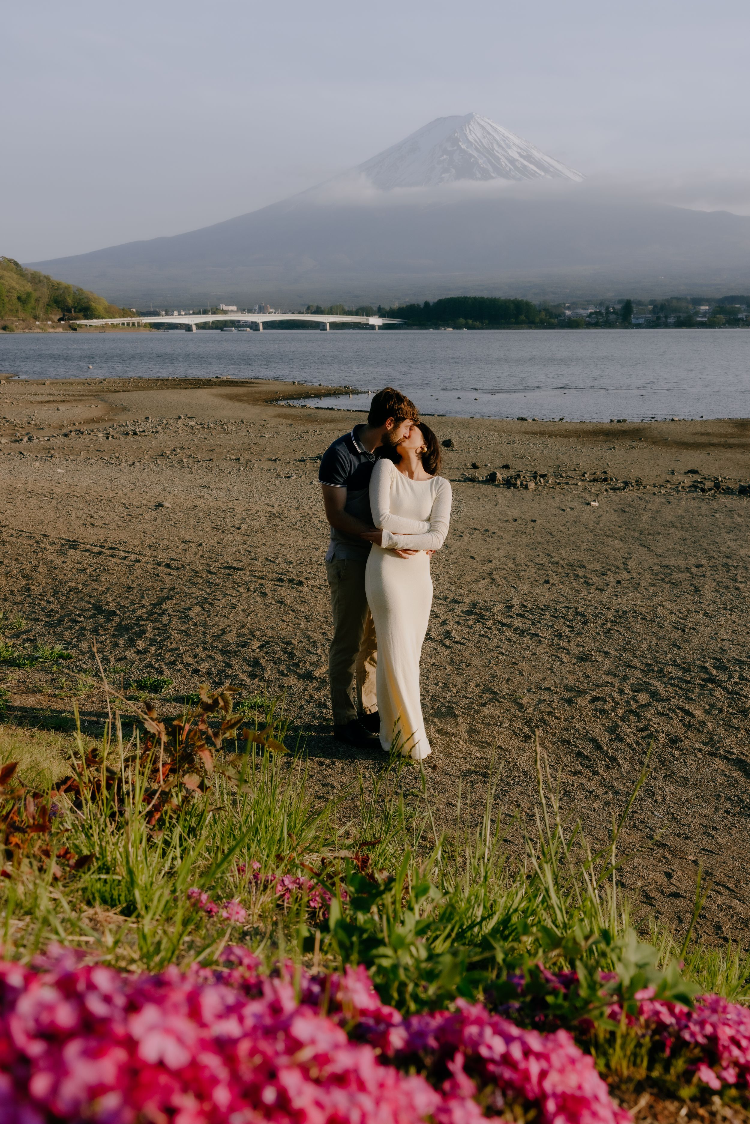 Mount Fuji creates a stunning backdrop for a romantic beach wedding photoshoot with pink flowers in the foreground.