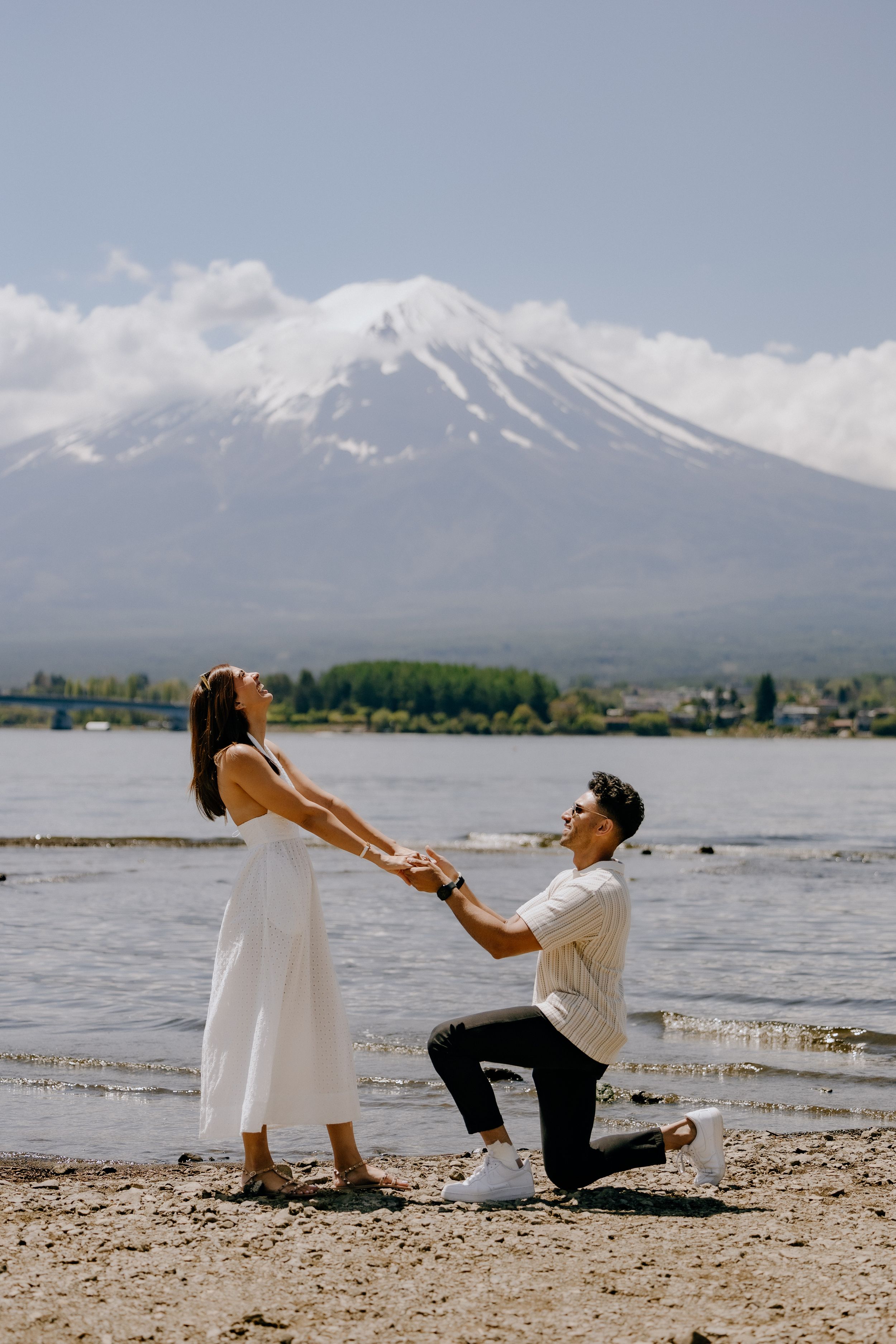 A romantic proposal scene on the shores of Lake Kawaguchiko with the snow-capped Mount Fuji in the background.