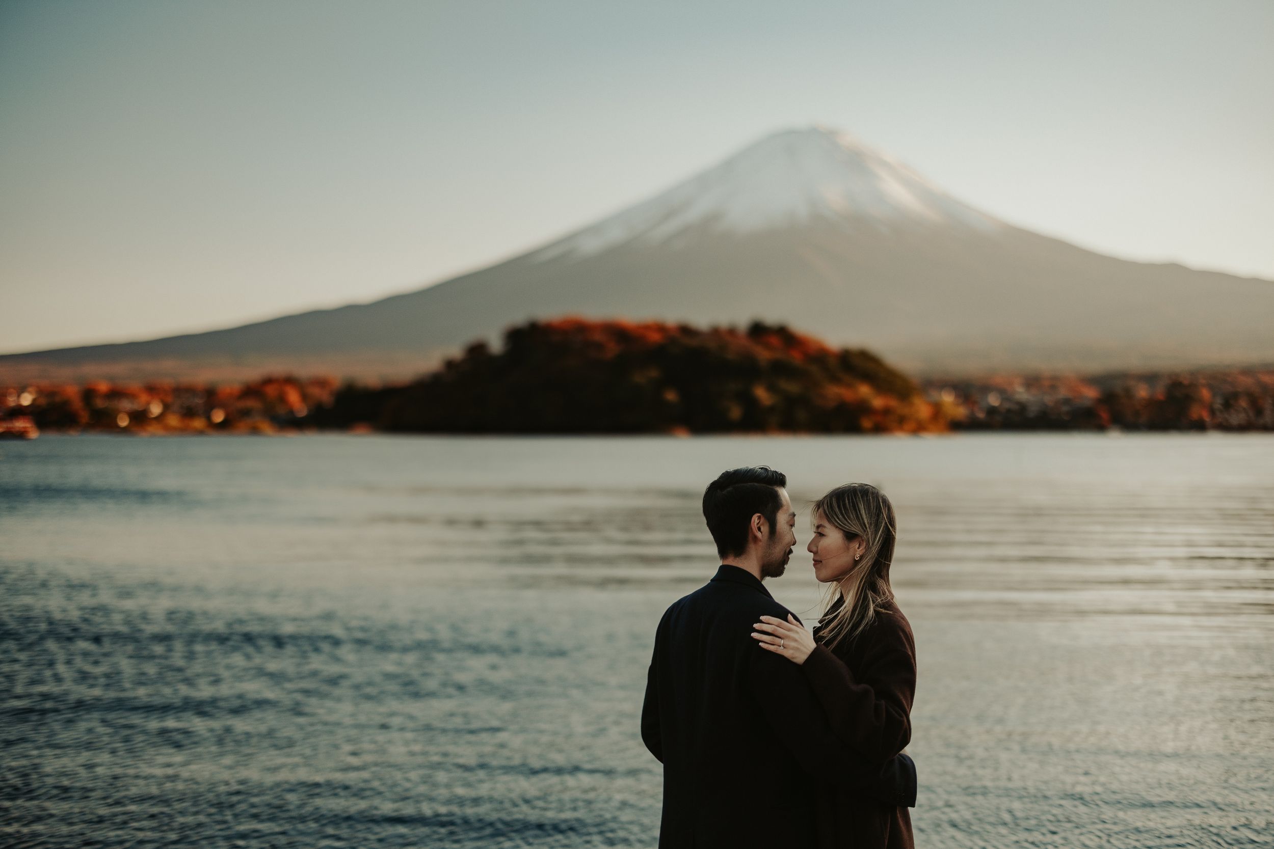 A scenic mountain view over a lake at sunset with silhouetted figures in the foreground.