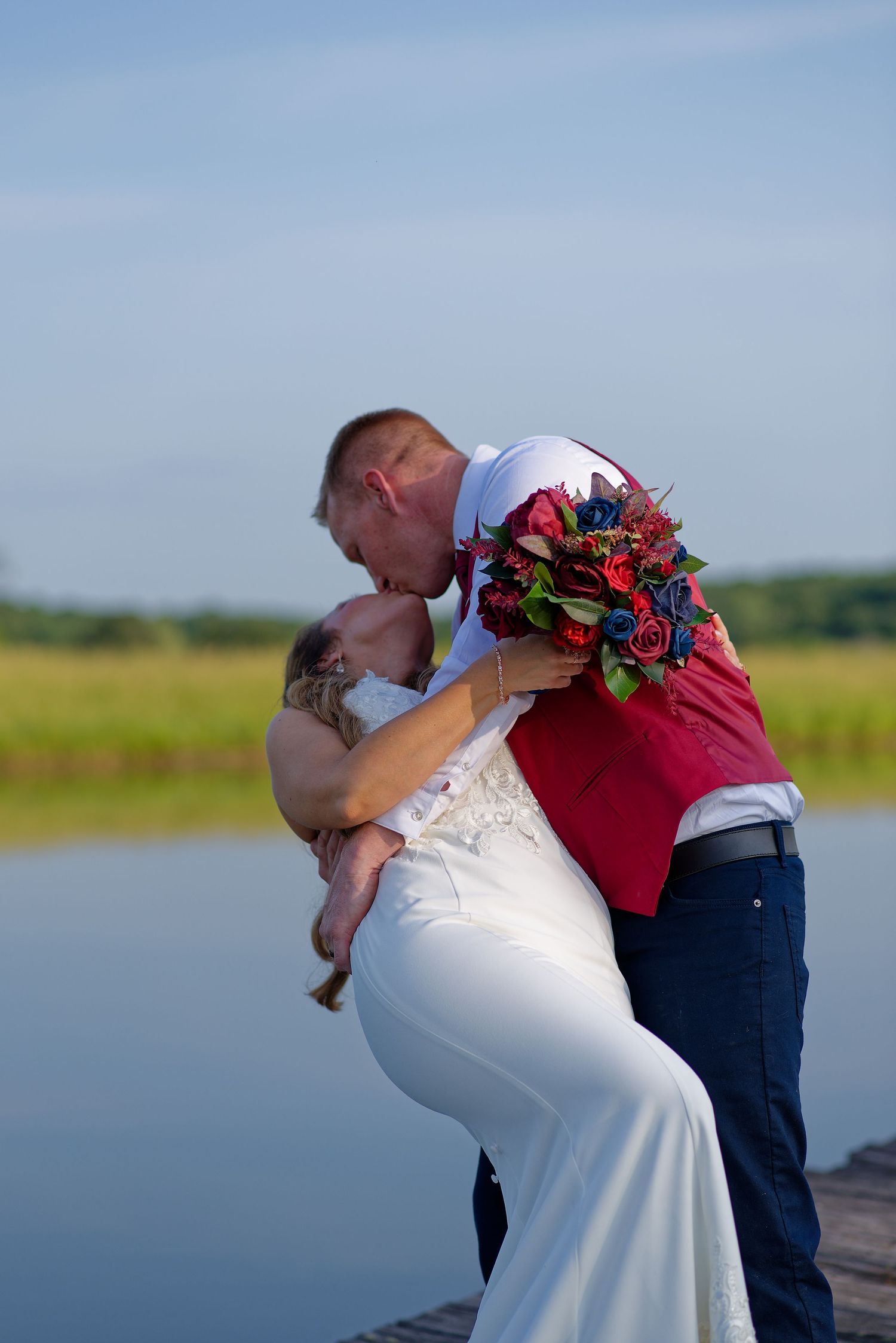 A romantic moment captured on a dock with a colorful bouquet as a couple embraces by the water on their wedding day.