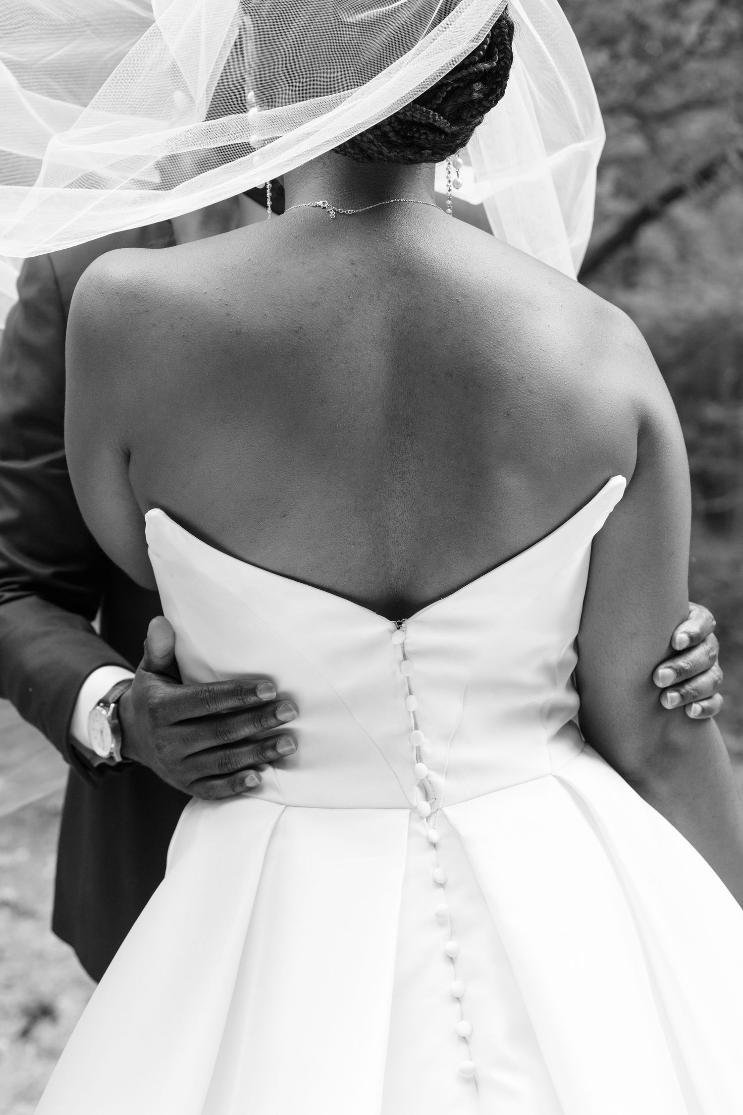 Black and white close-up of bride's button-back wedding gown with groom's hands on her waist.