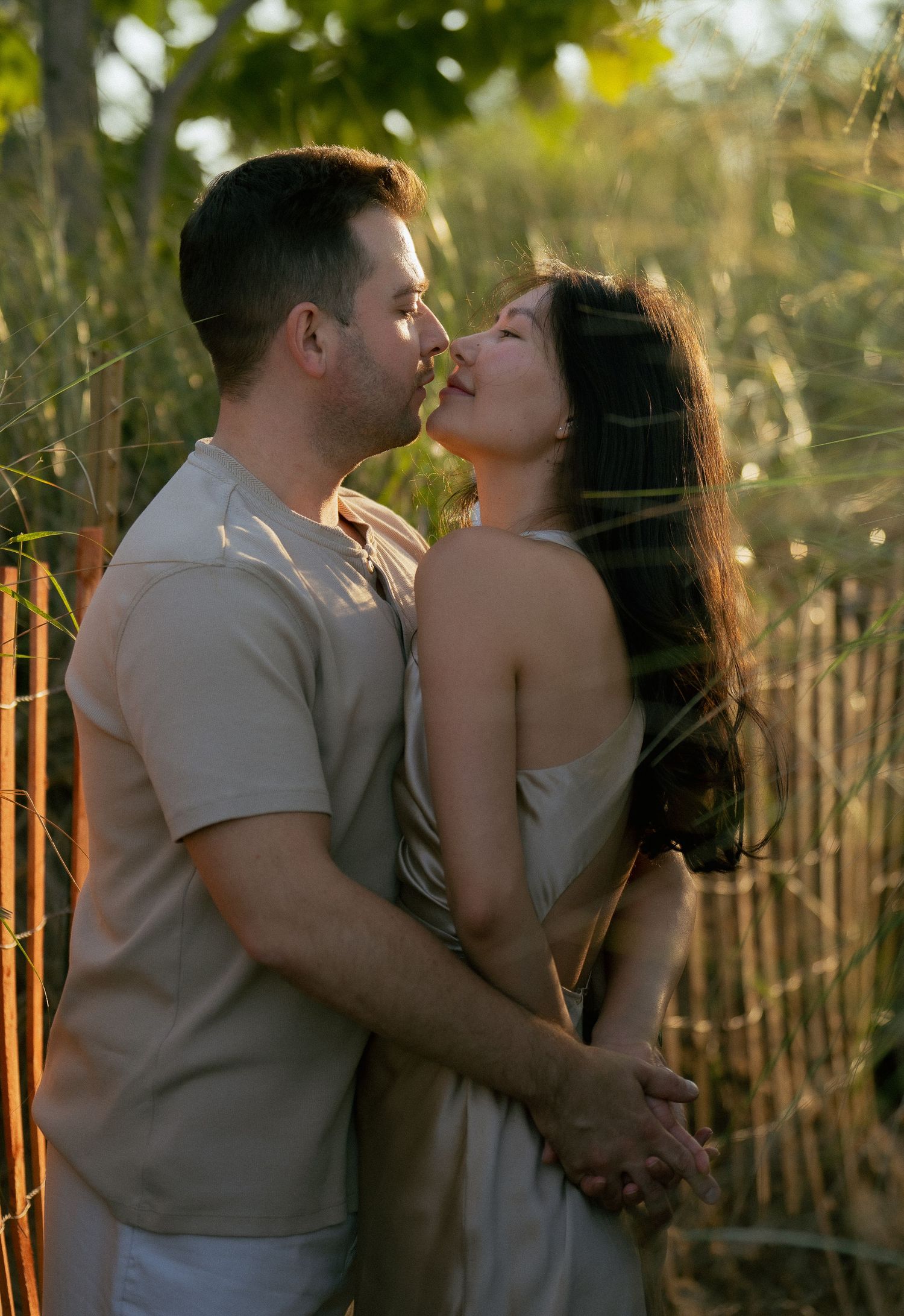 A romantic couple shares an intimate moment against a natural fence during golden hour.