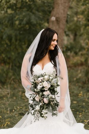 Bride in lace gown holding white and green bouquet during outdoor photo session.