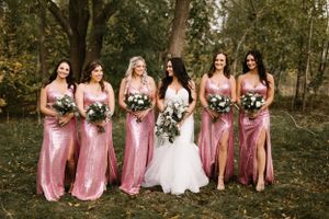 Bridesmaids in pink sequin dresses pose with bride in white gown outdoors.