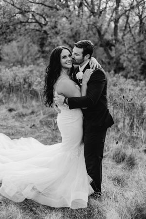 Black and white portrait of newlyweds embracing in outdoor setting.