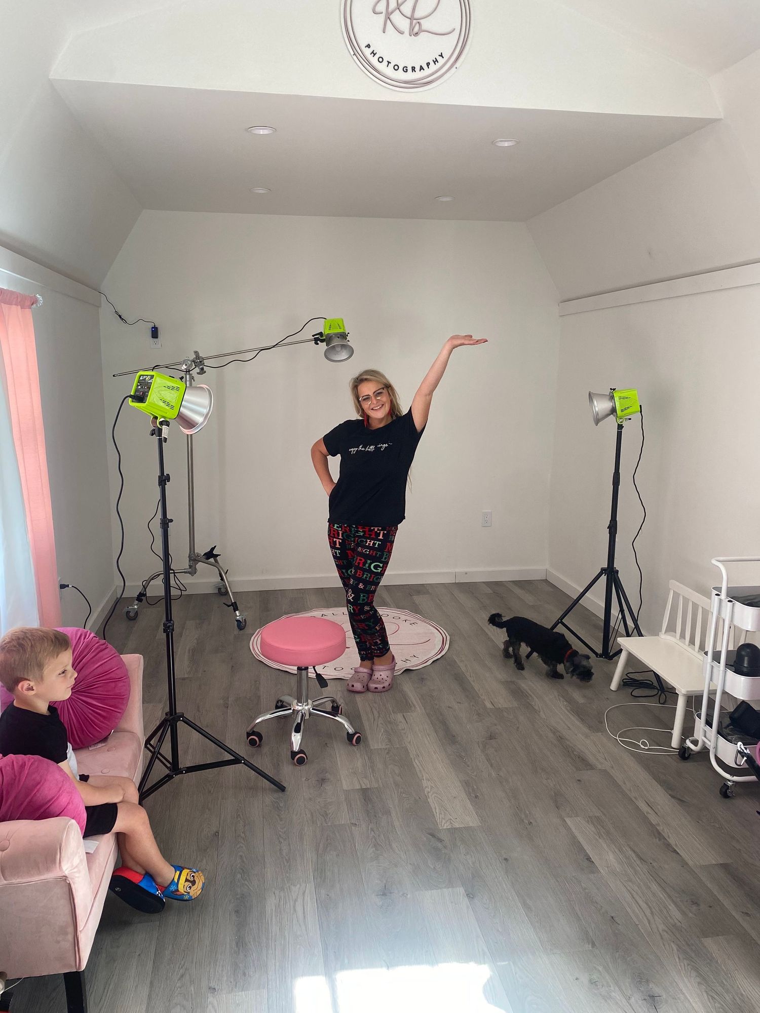 A photography studio setup with neon lights, gray flooring, and a pink stool showing a dance or modeling pose.