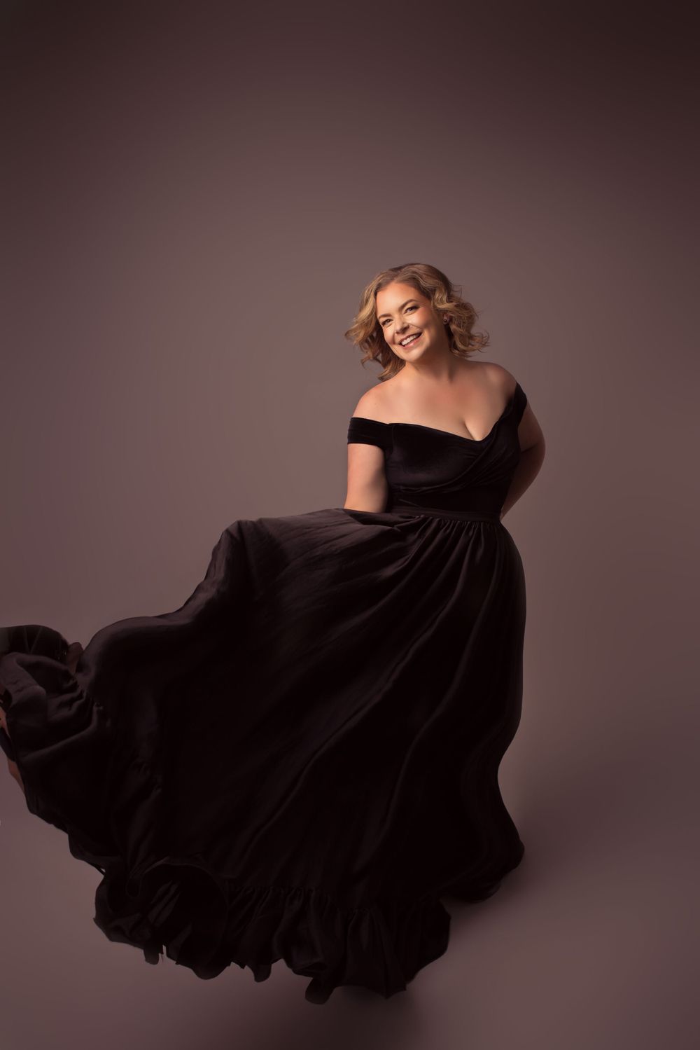 Elegant portrait in flowing black velvet gown with off-shoulder neckline.