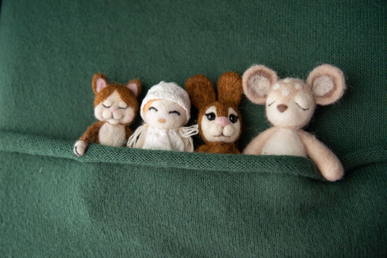 Four cute felt animal toys including cat, bunny, bear, and mouse peeking over green fabric.