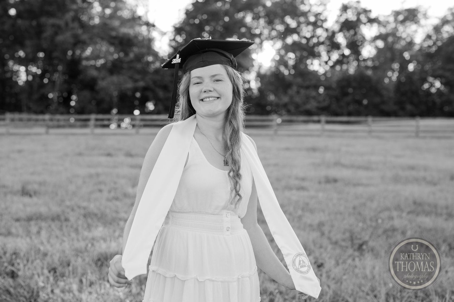 Black and white photo of graduate laughing in pastoral setting with fence.
