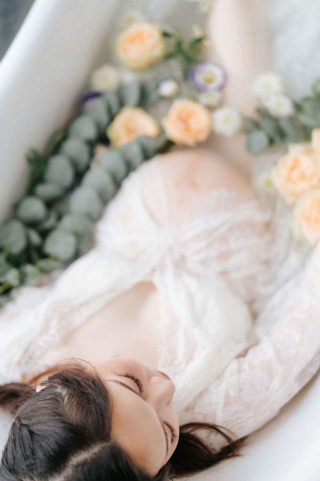Ethereal portrait with peach roses and eucalyptus branches in white bathtub setting.