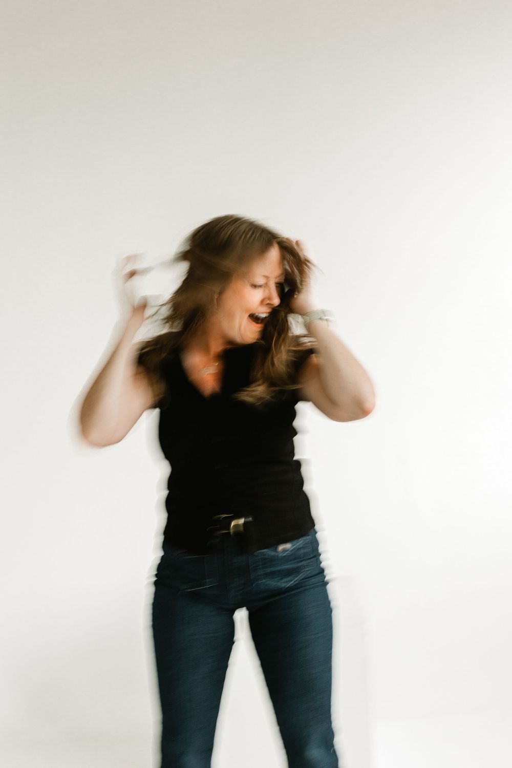 Blurred motion photo of a woman in black top and jeans tossing her hair expressively.