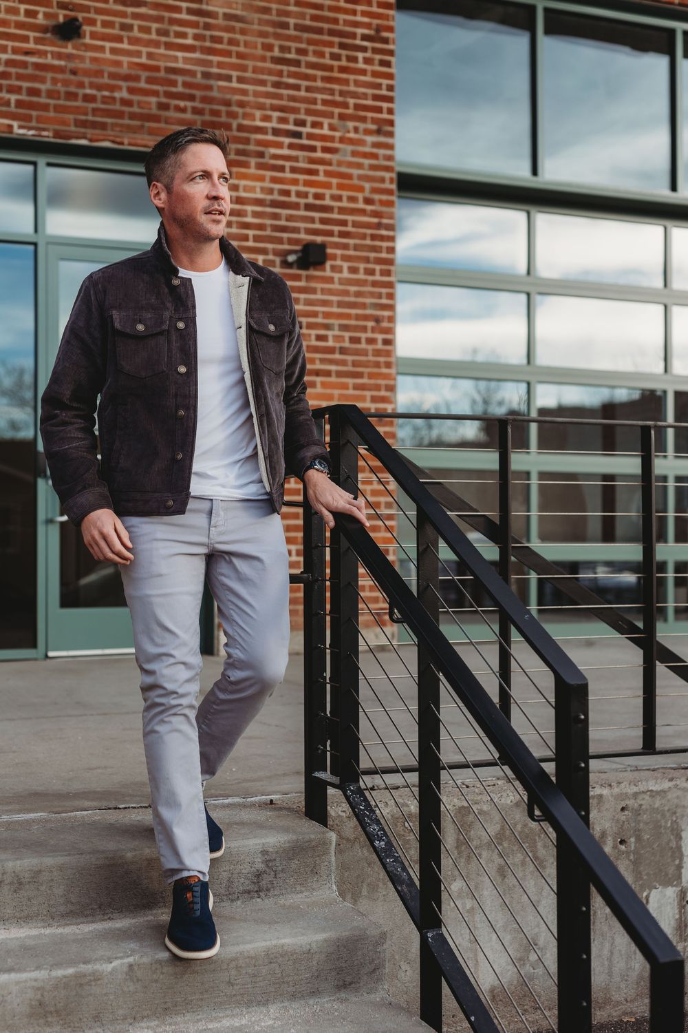 Man in dark jacket and gray pants walking down outdoor steps near a brick building.