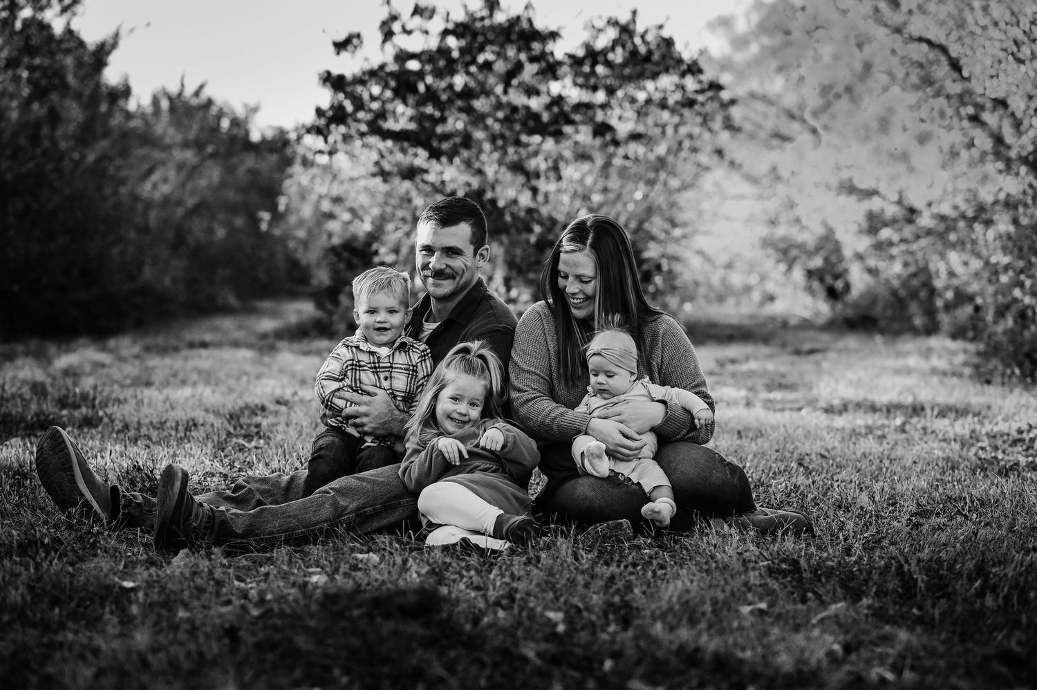 Black and white photo of a loving family sitting together outdoors on the grass during a photo session in nature.