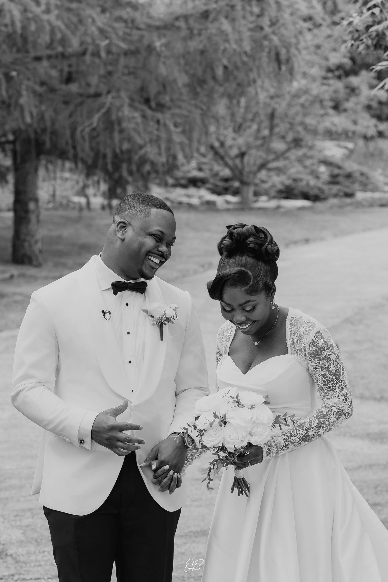 A loving couple shares a joyful moment in black and white on their wedding day, wearing elegant white attire.