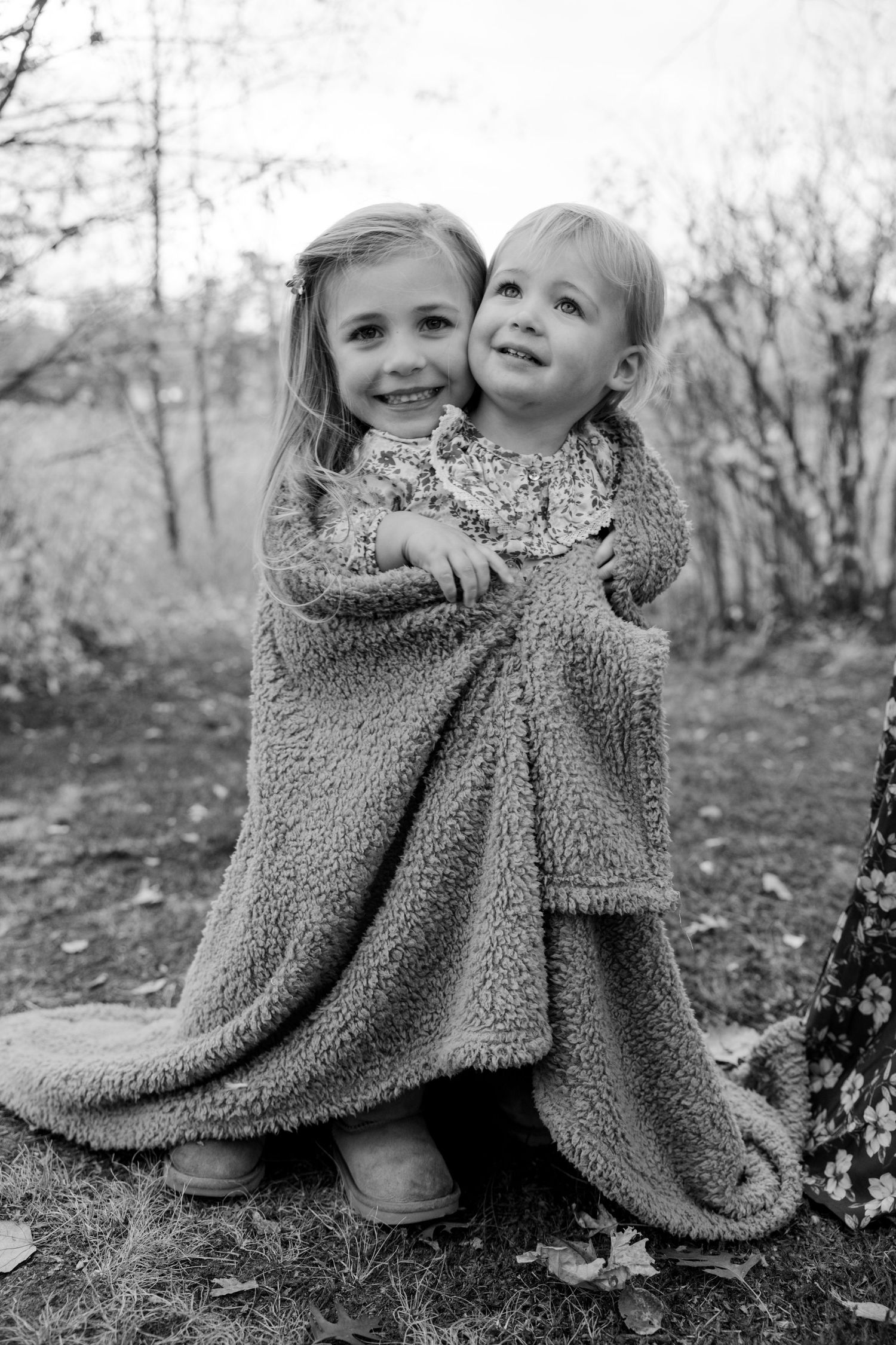 Two children wrapped in a cozy blanket share a sweet moment outdoors.