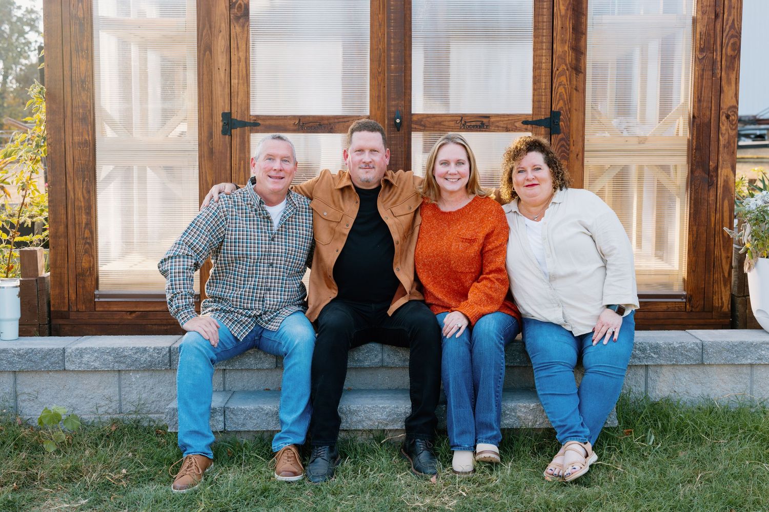 Group sitting together on outdoor bench against wooden window frame.