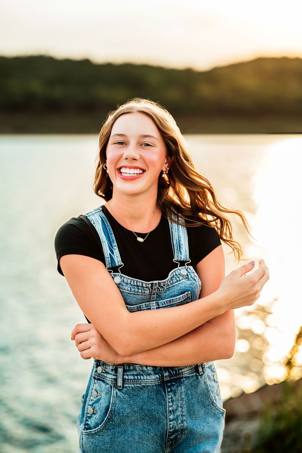 Golden hour portrait in denim overalls against a serene lake backdrop.