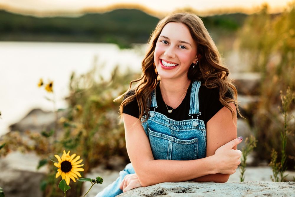 Summer portrait with sunflowers by the water wearing denim overalls.