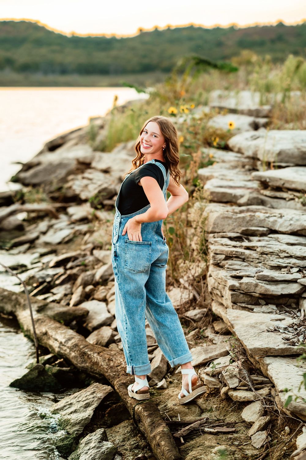 Casual figure explores rocky lakeside terrain while wearing denim and black top during golden hour.