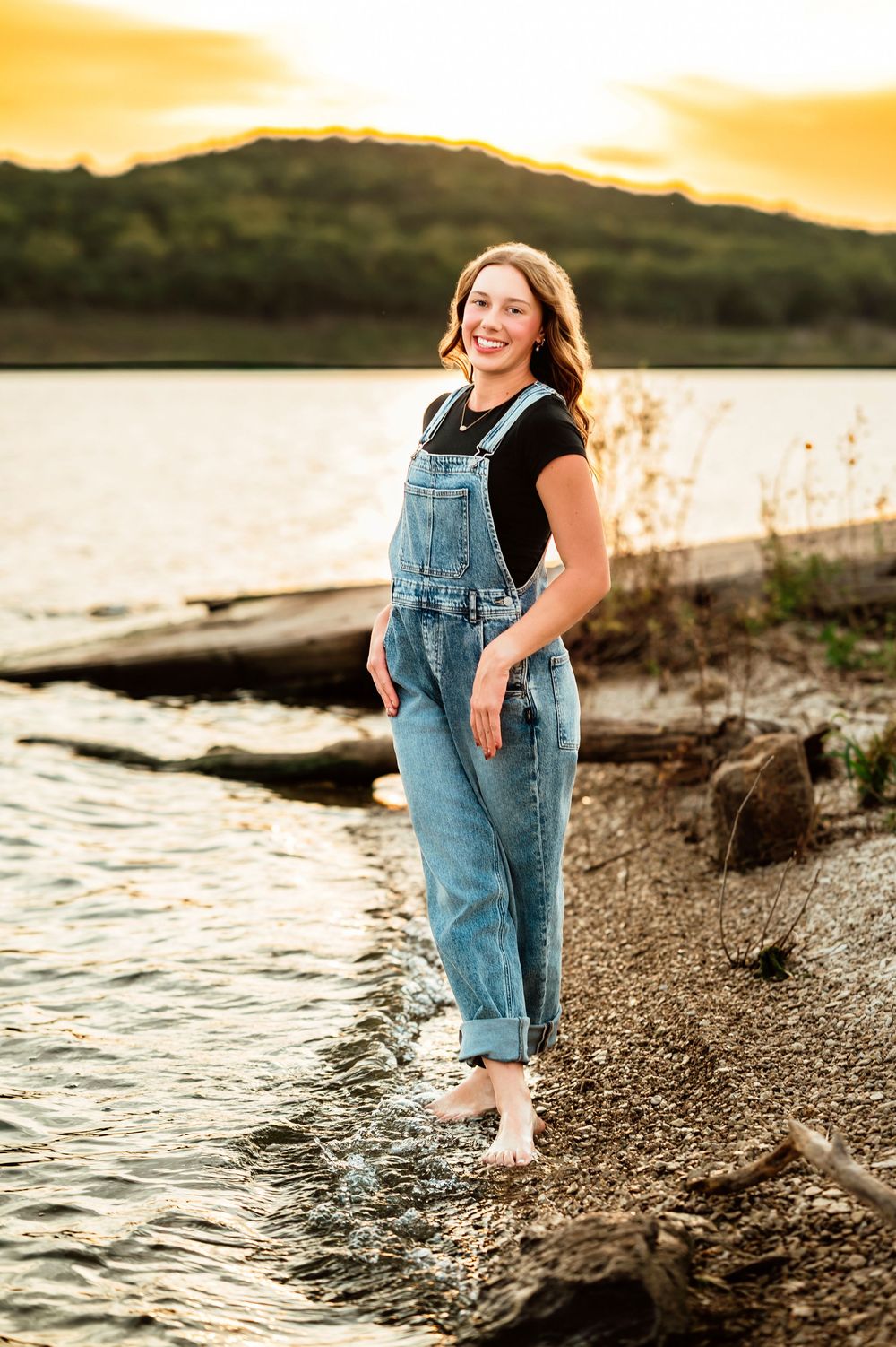 Casual sunset portrait by the water wearing denim overalls and a black t-shirt.
