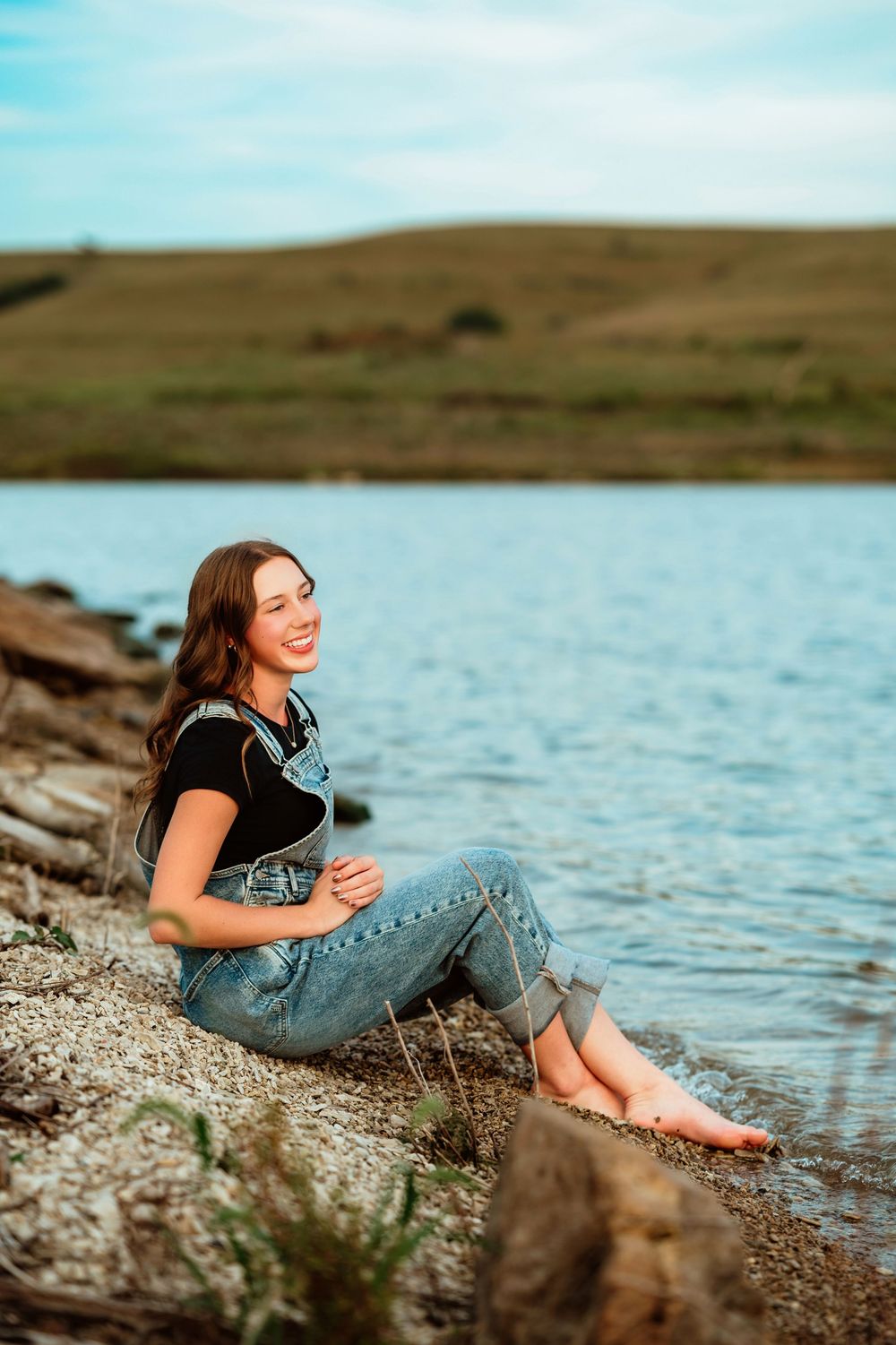 Relaxed scene by the water with someone lounging on rocky shore wearing denim and black top.