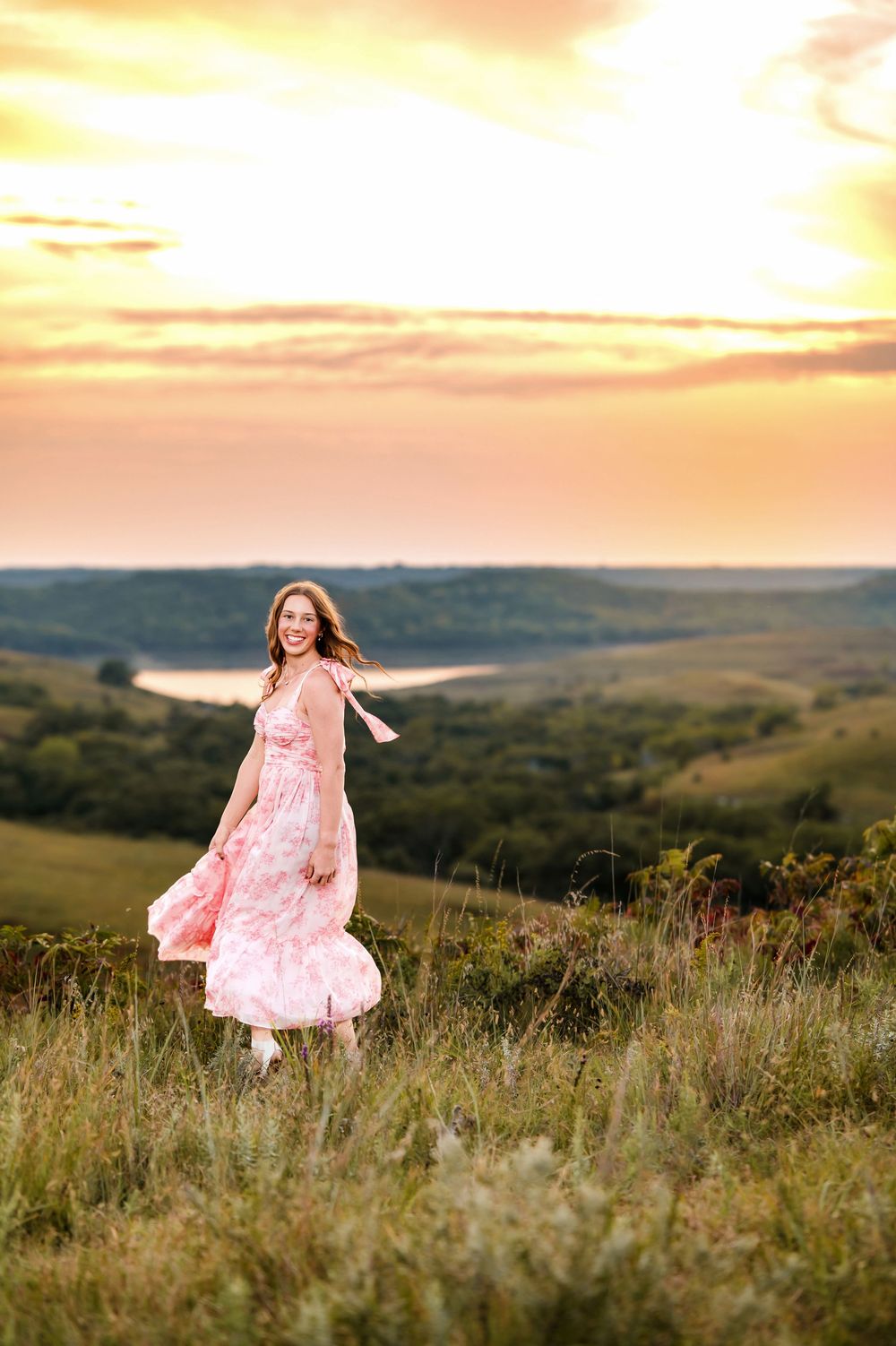 A pink floral dress twirls against a scenic hilltop landscape during golden hour sunset.