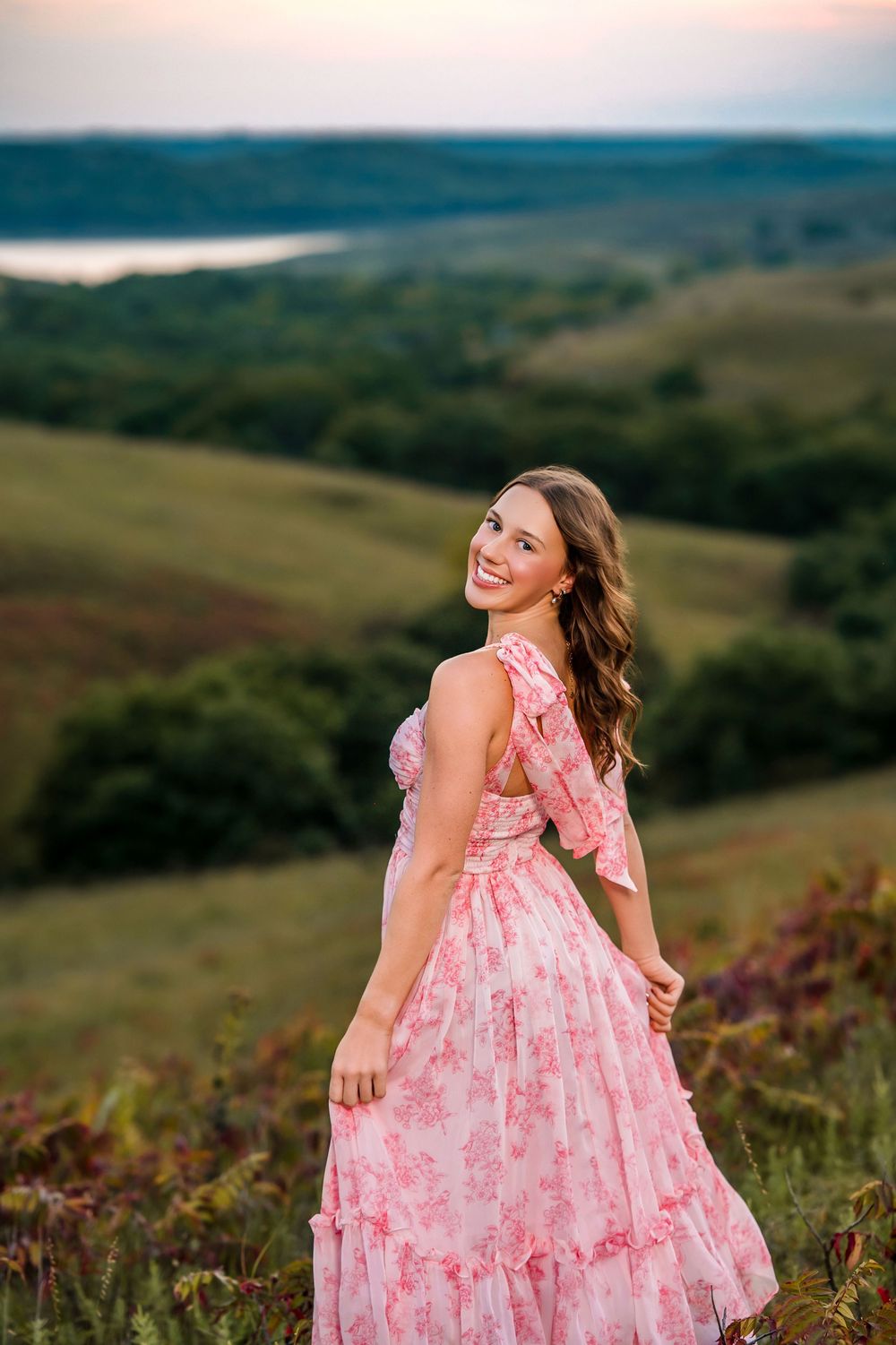 Twirling in pink floral dress on rolling hills during golden hour.