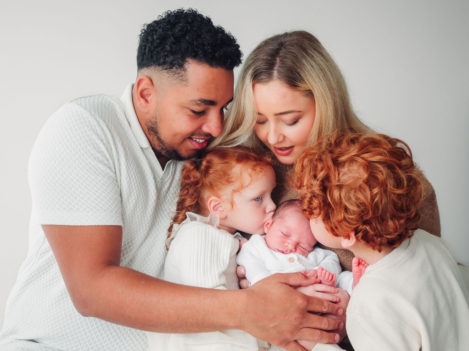 A mixed couple with their two older children cuddle together with their newborn baby - photographed by Verity Photography on a training day