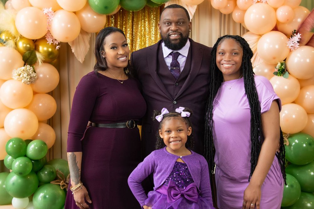 Family celebration photo with peach and green balloon arch decorations in the background.