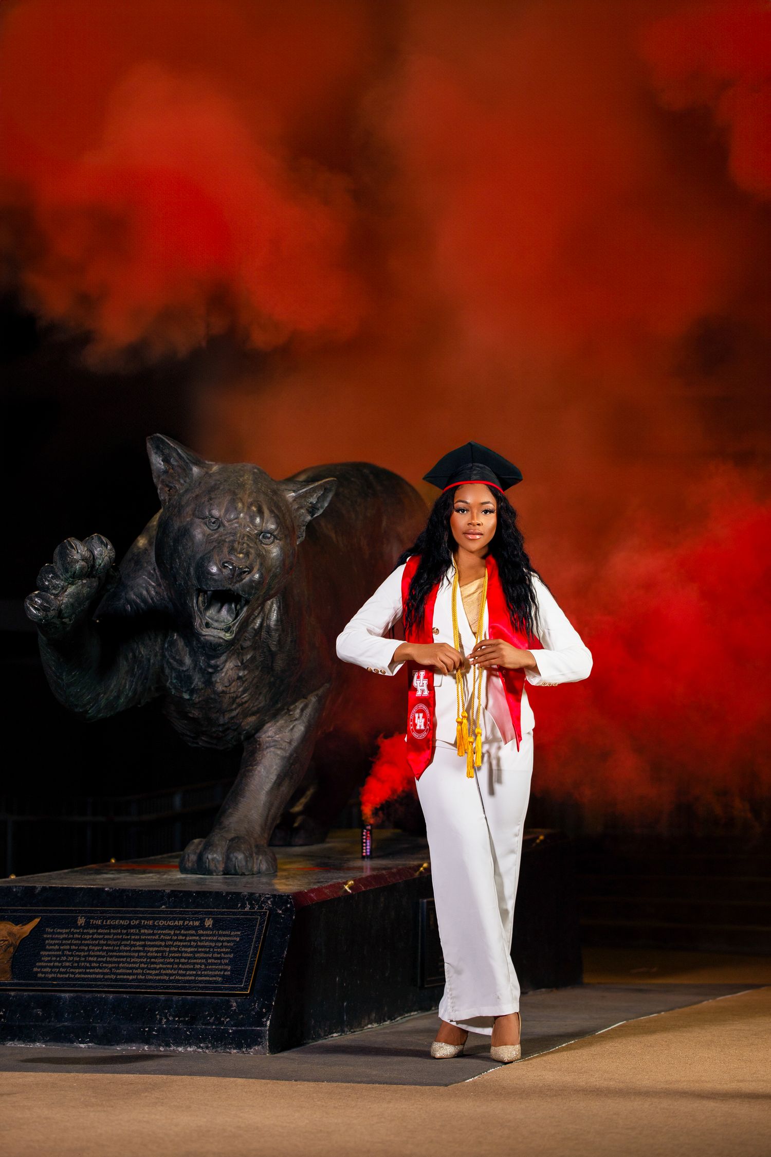 Graduation photo at university of houston cougar statue with red dramatic smoke bomb in the background.