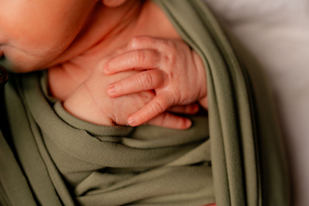 Close-up of tiny newborn baby feet wrapped in soft olive green blanket.