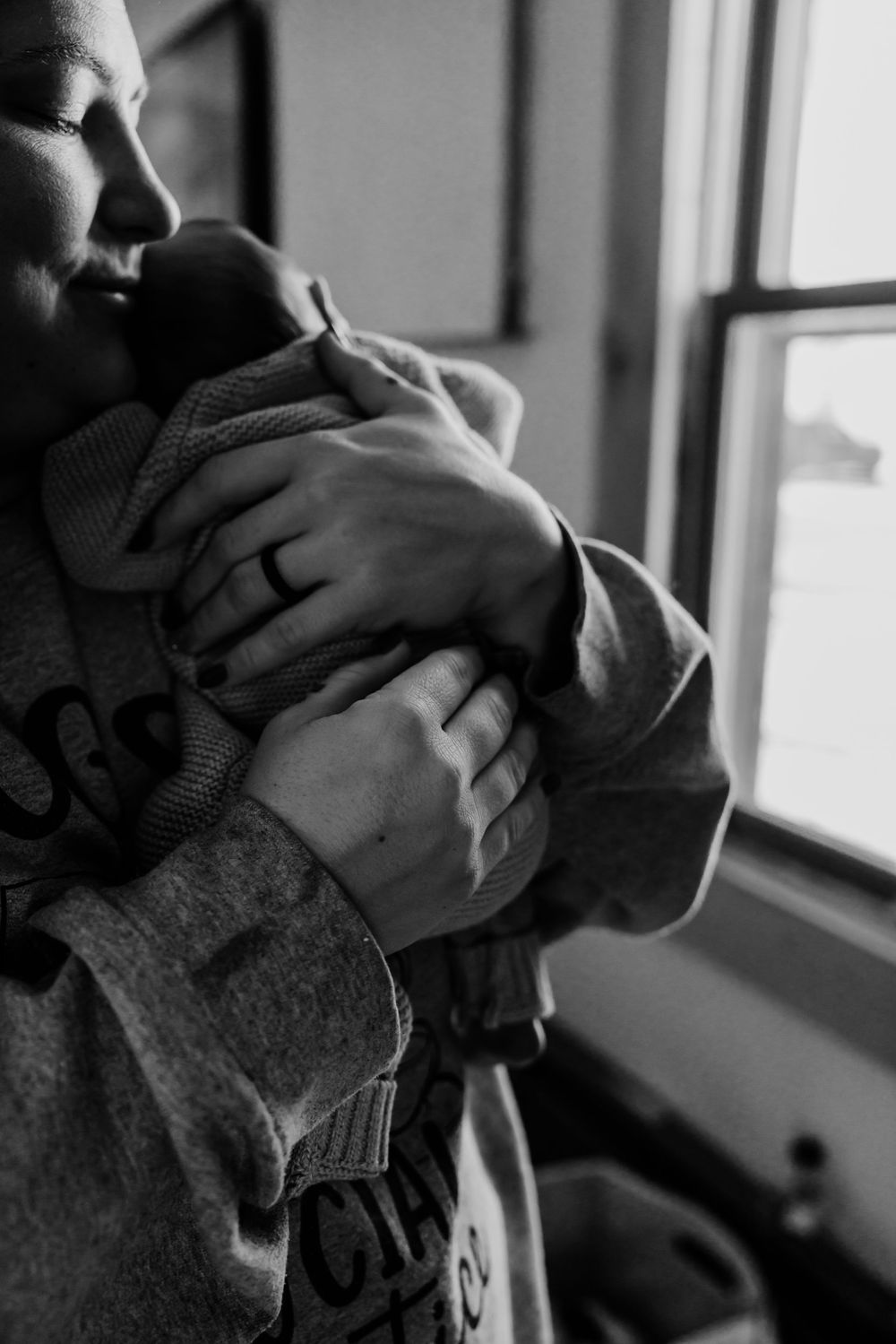 Closeup black and white photograph shows hands gently cradling a pet cat in front of a window.