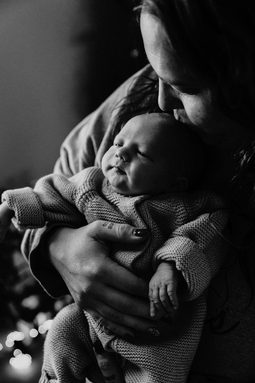 A tender black and white photo of a sleeping infant being cradled in loving arms, wrapped in a knit sweater.