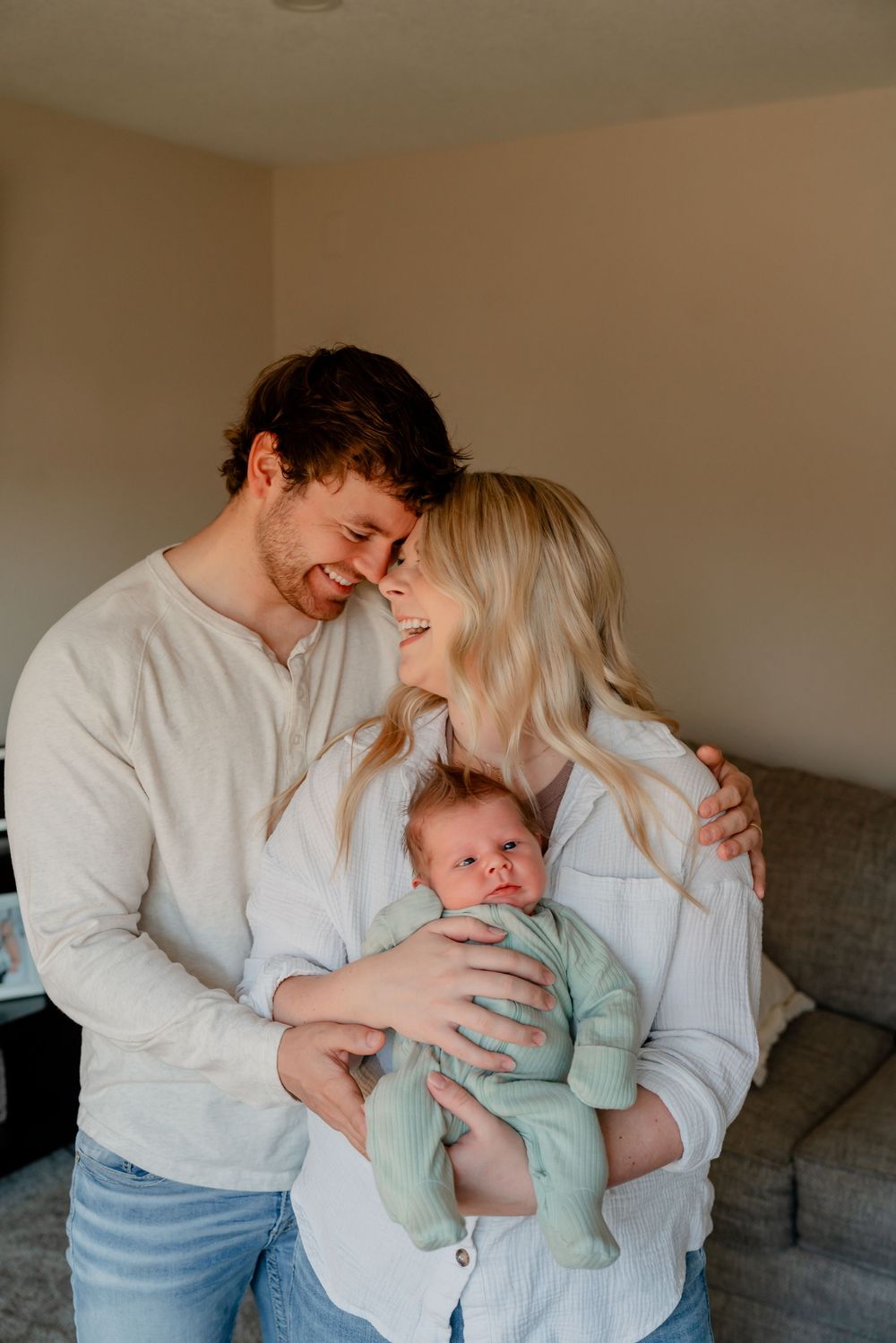 A couple shares a joyful moment with their baby in a cozy living room setting.