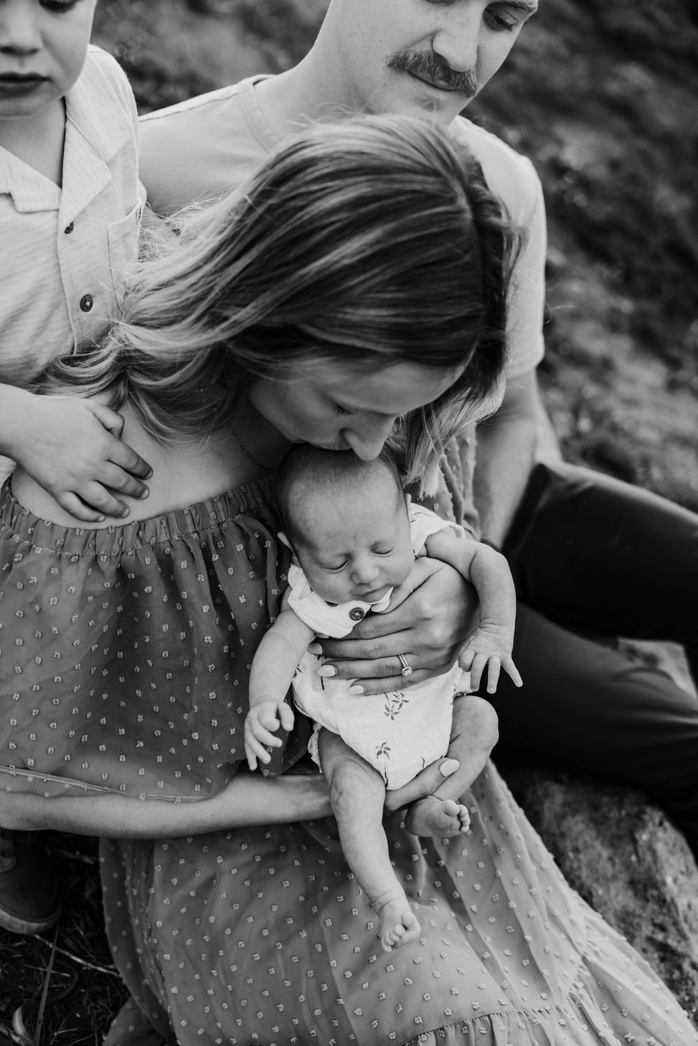 A tender black and white family portrait shows a moment of connection with a small baby outdoors in nature.