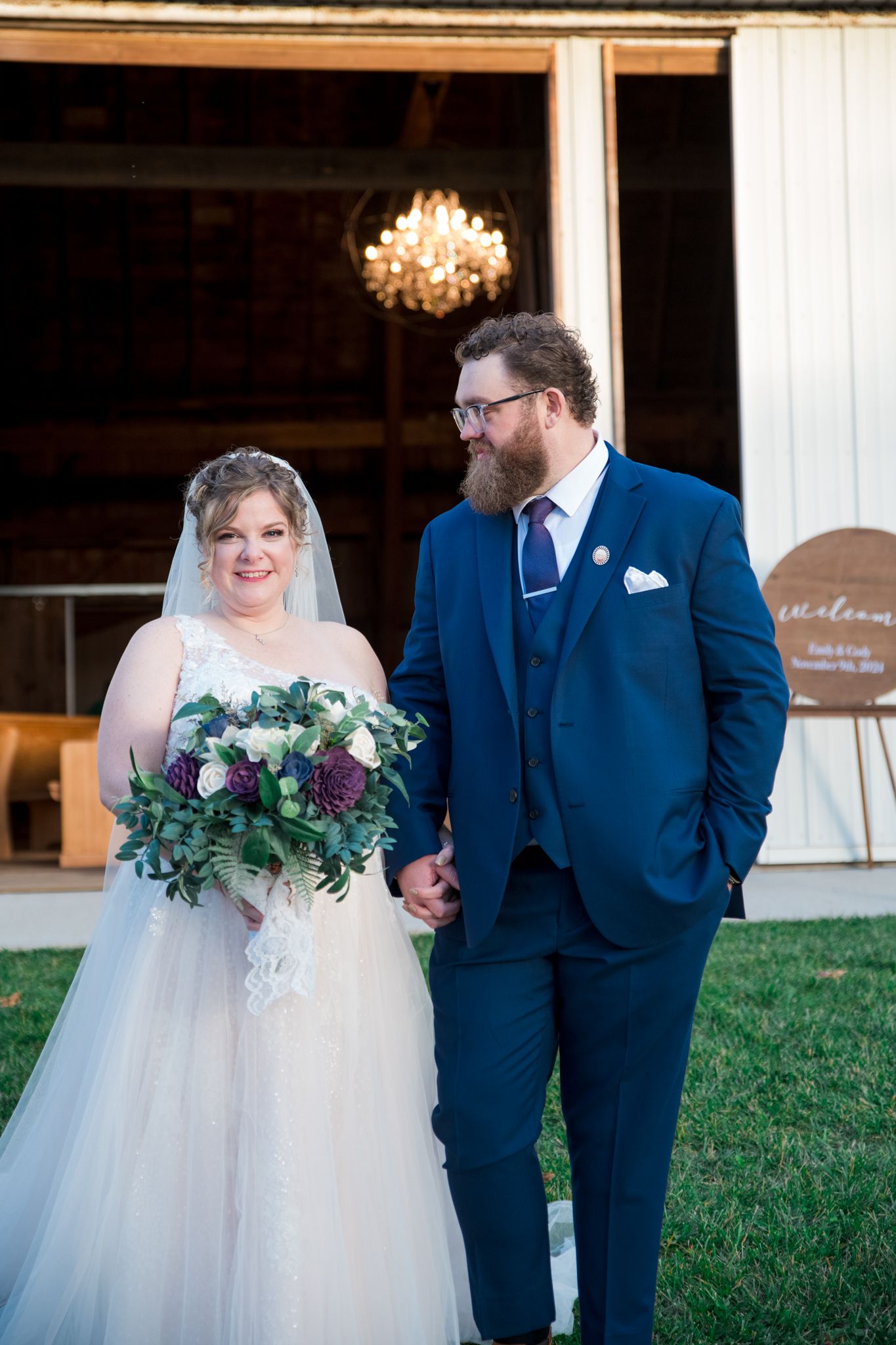 A wedding couple standing outside a rustic barn venue at dusk.
