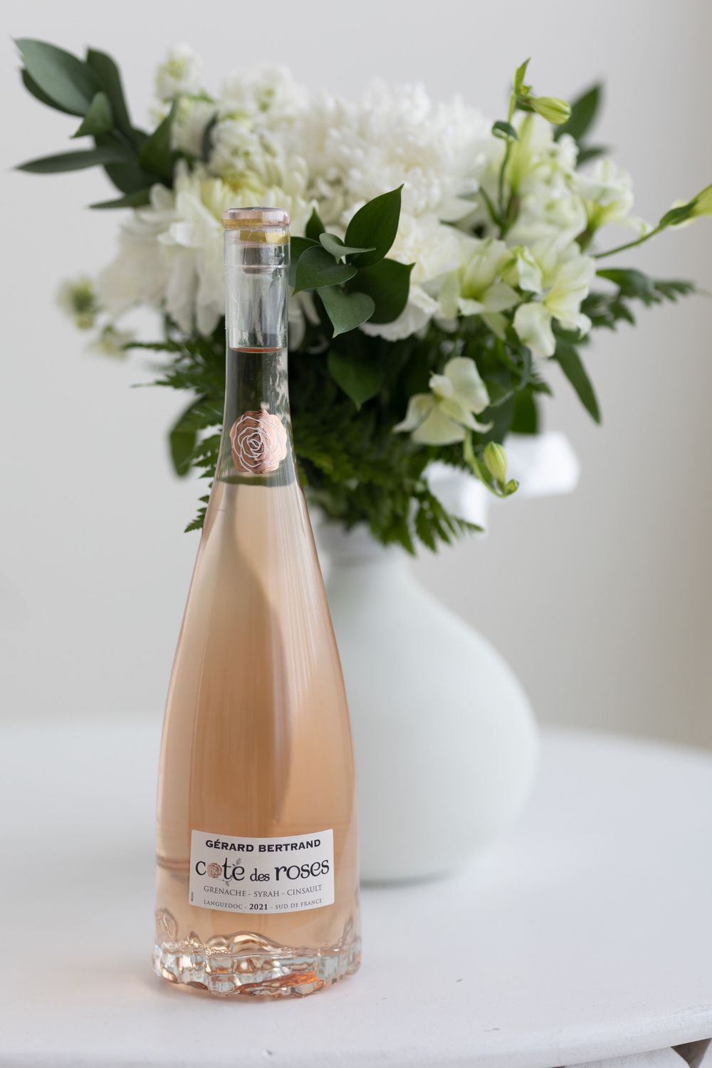 Bottle of Gerard Bertrand Cote des Roses rose wine in front of white flower bouquet.
