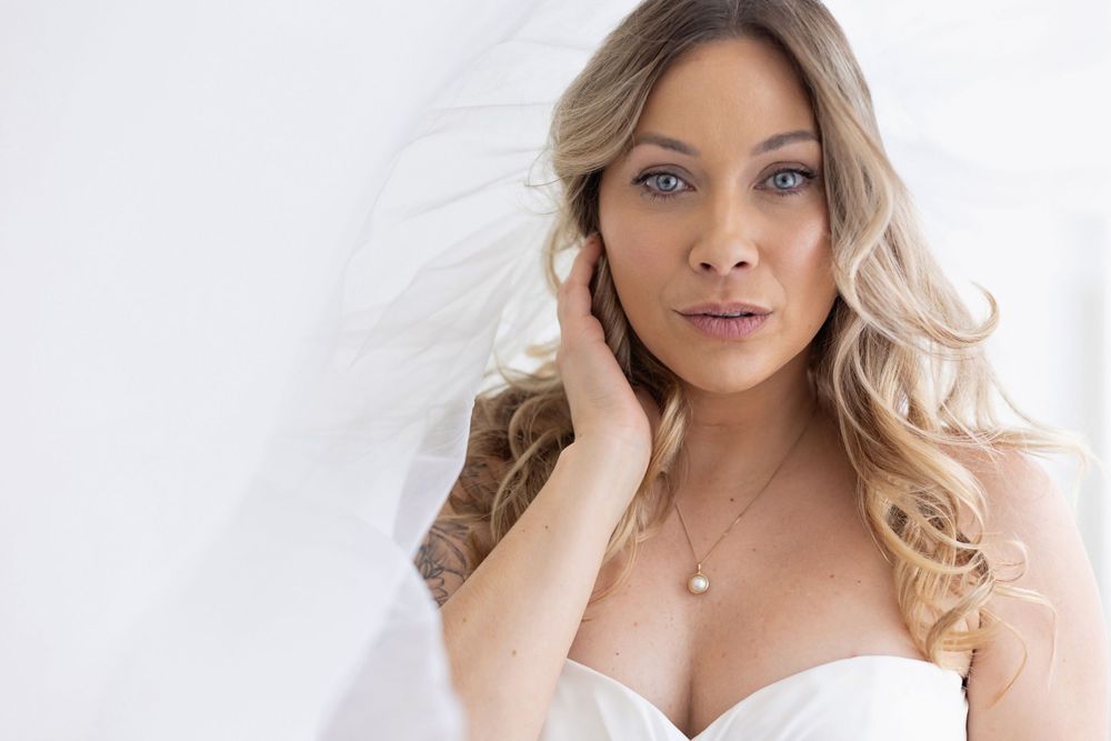 Close-up portrait of blonde bride in strapless dress with veil touching her face.
