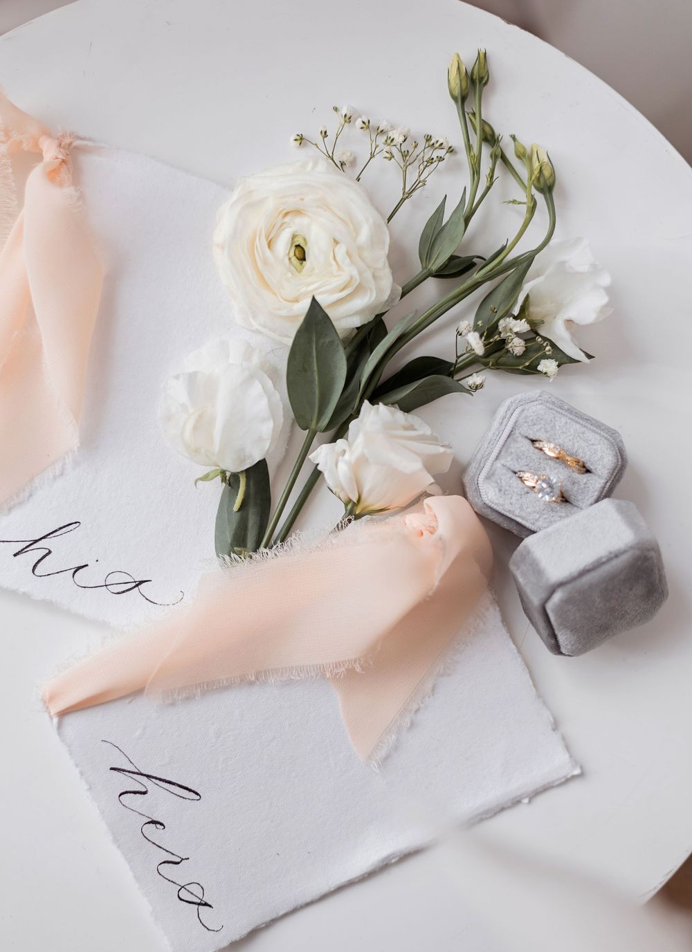 Elegant wedding flat lay with white roses, peach ribbons, ring box, and calligraphy cards.