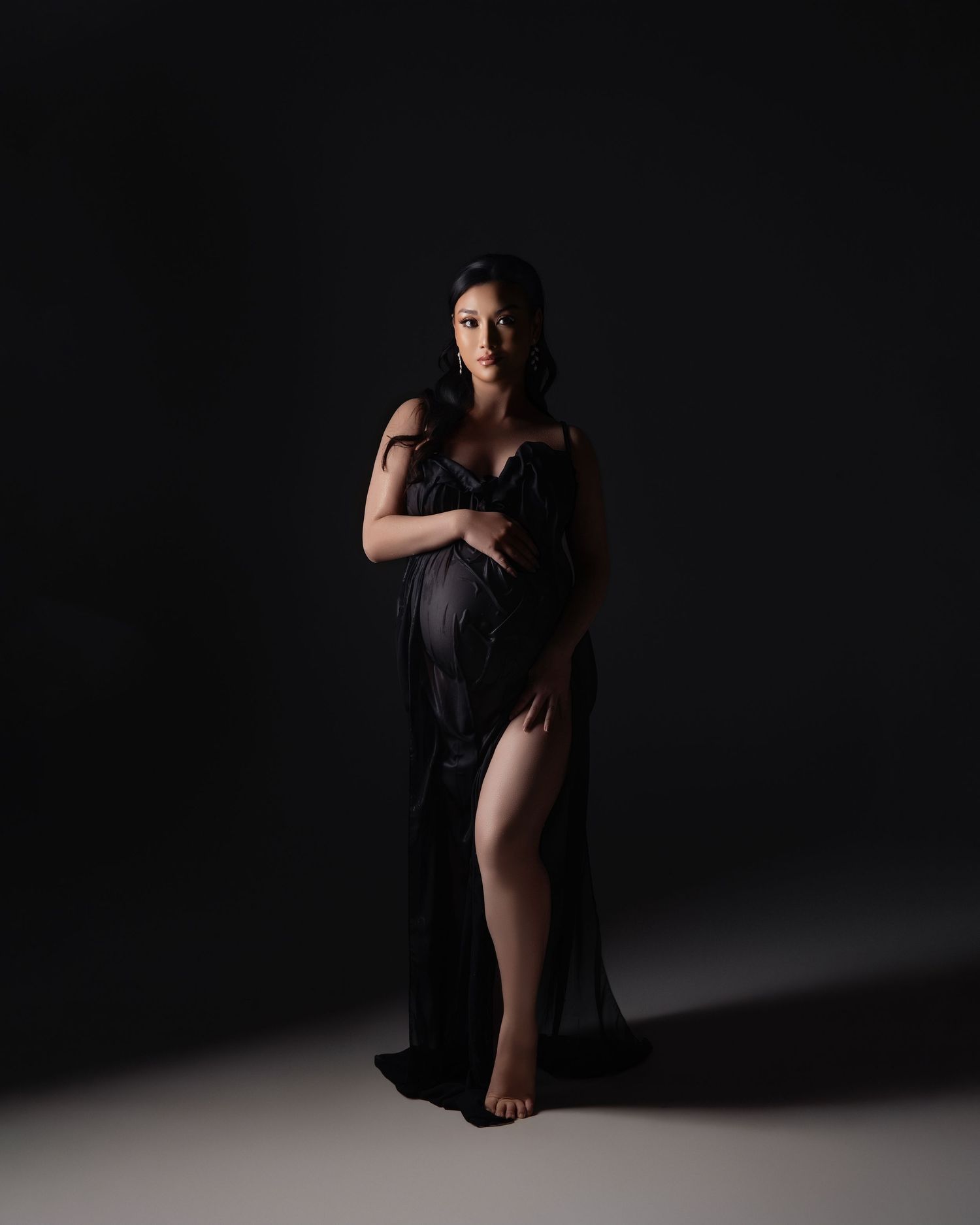 Artistic portrait photography of figure in flowing black dress against dark background with dramatic lighting and contrast.