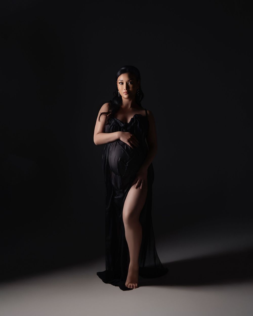 Artistic portrait photography of figure in flowing black dress against dark background with dramatic lighting and contrast.