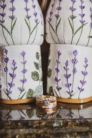A diamond ring displayed on rustic wood with a floral patterned fabric featuring purple lavender stems in the background.