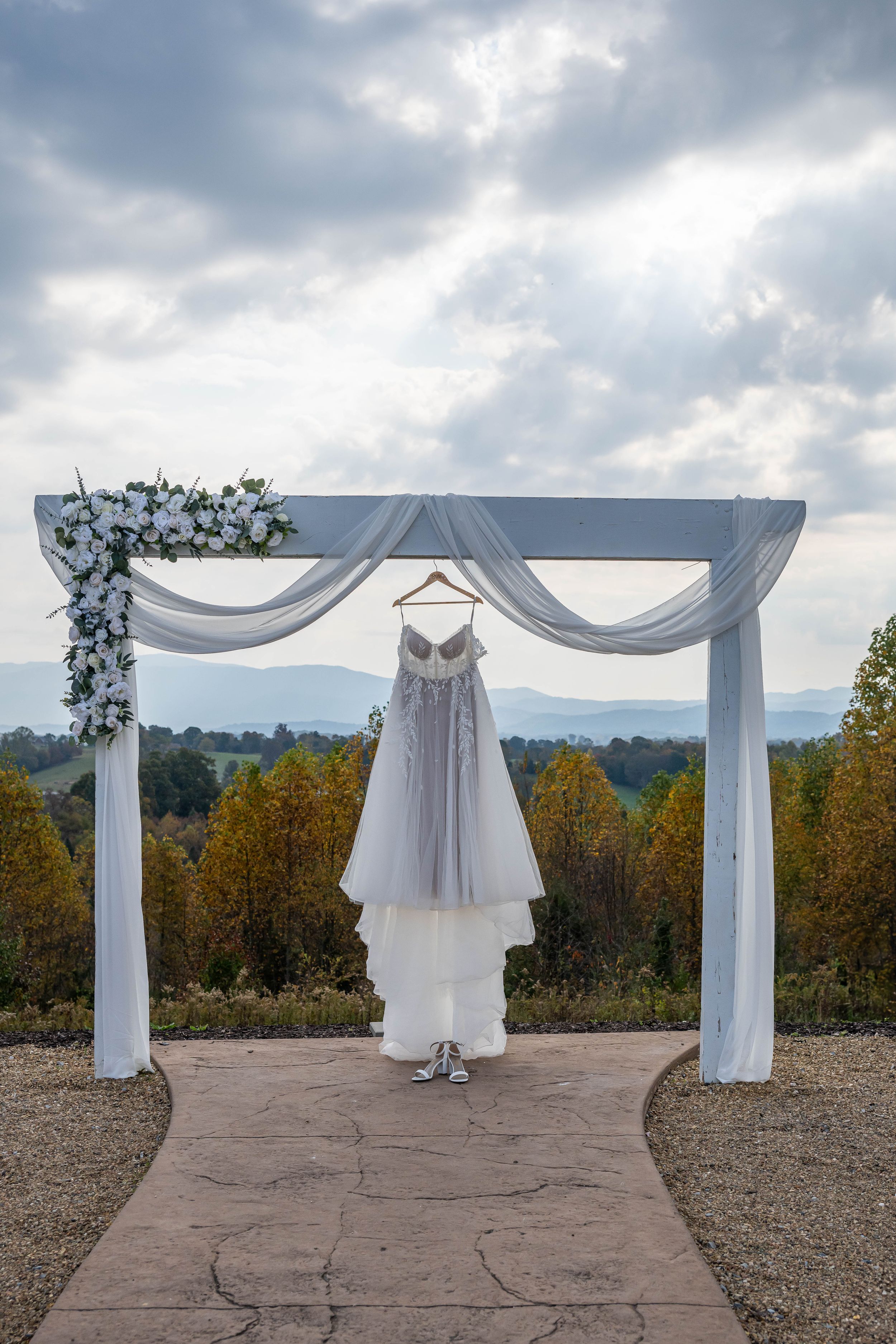 White wedding dress hanging on decorated arch with mountain view backdrop.