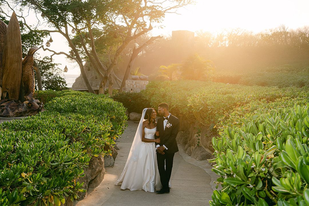 A tender moment between a couple under an archway decorated with pink flowers and greenery.