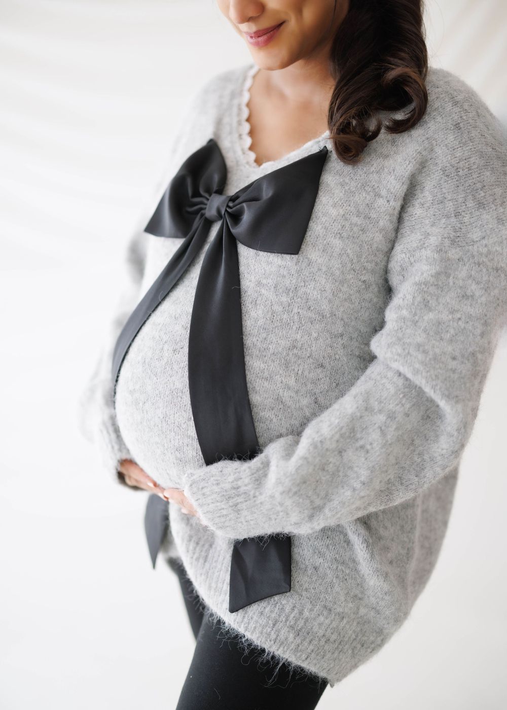 Close-up of a cozy grey sweater with black bow detail and pearl necklace.
