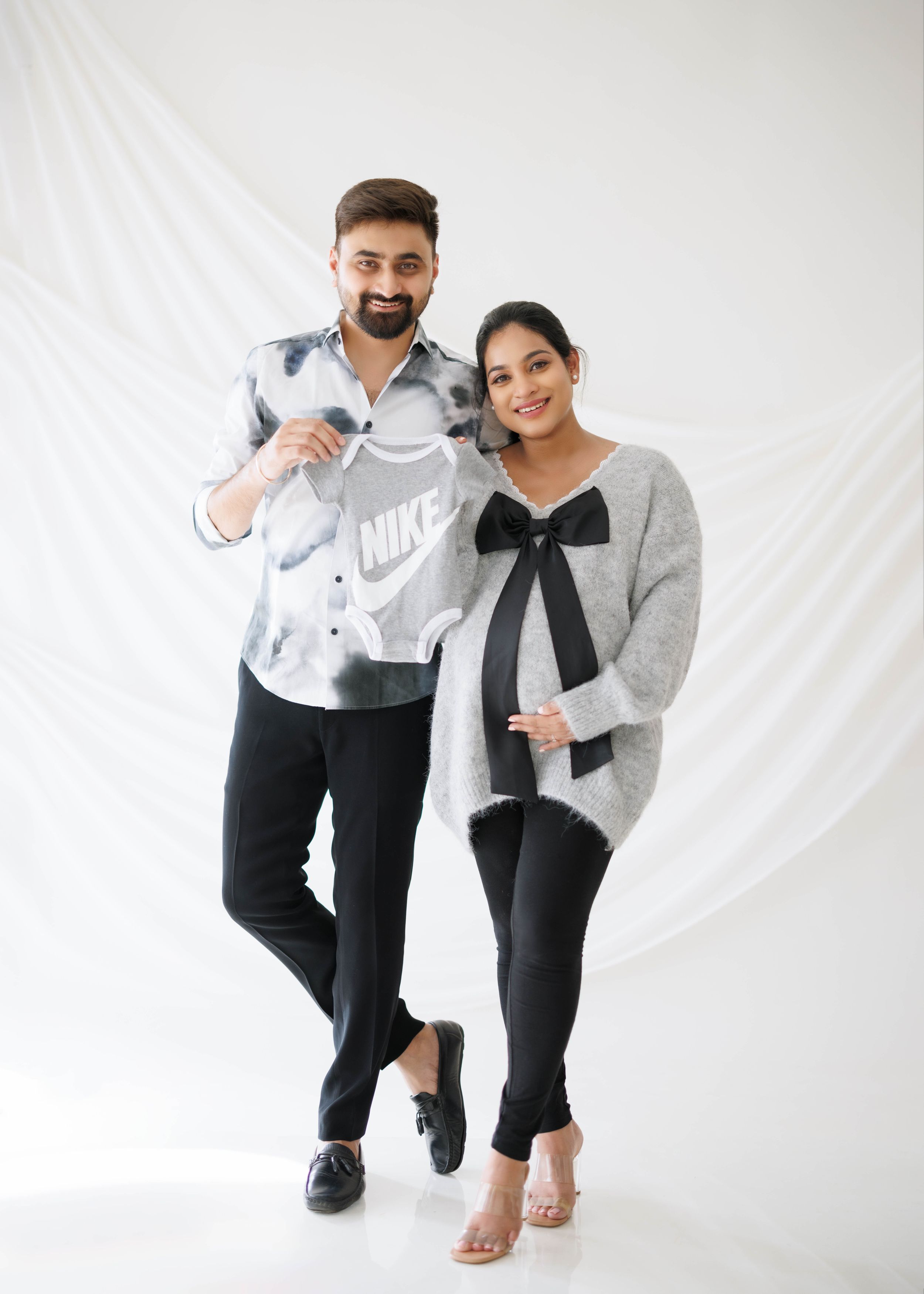 Couple posing in casual attire against white backdrop during maternity photoshoot.
